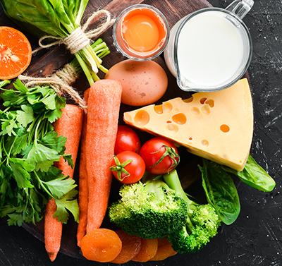 Foods containing natural Vitamin A: broccoli, carrots, milk, cheese, spinach, apricots, parsley, tomatoes. On a black stone kitchen background. Top view.